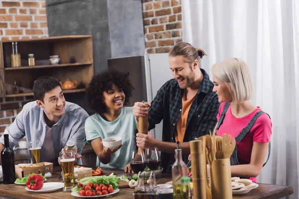 Multiethnic friends looking how man adding spice to food with pepper grinder — Stock Photo