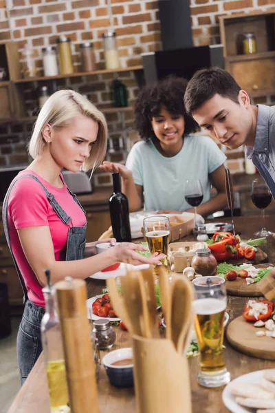Amigos multiétnicos mirando con sorpresa en la mesa con comida - foto de stock
