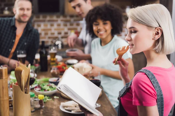 Girl holding recipe book and biting wooden spatula — Stock Photo