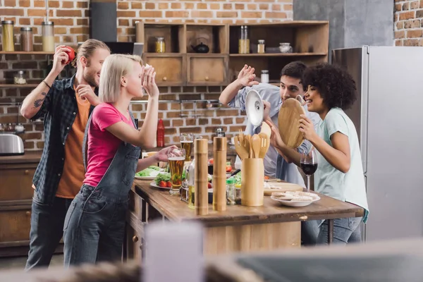 Amigos multiétnicos jugando con la comida en la cocina - foto de stock