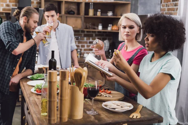 Amigos multiétnicos cocinar con libro de recetas - foto de stock