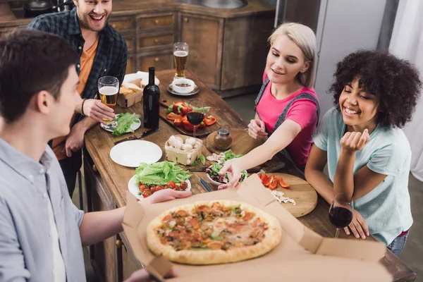 Мужчина показывает домашнюю пиццу многонациональным друзьям — стоковое фото