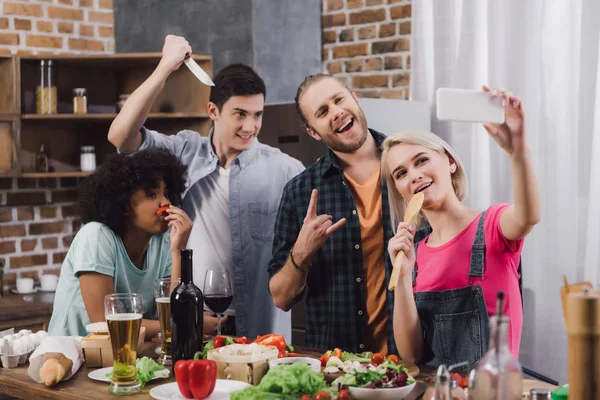 Улыбающиеся мультикультурные друзья делают селфи со смартфоном на кухне — стоковое фото