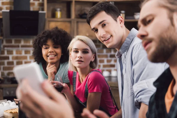 Multiethnic friends looking at smartphone in kitchen — Stock Photo