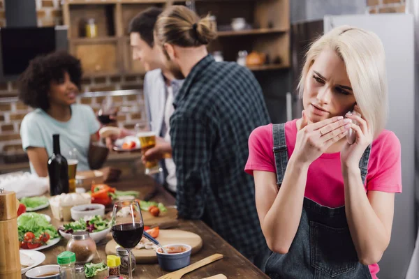 Verärgertes Mädchen spricht per Smartphone, während multiethnische Freunde Spaß haben — Stockfoto