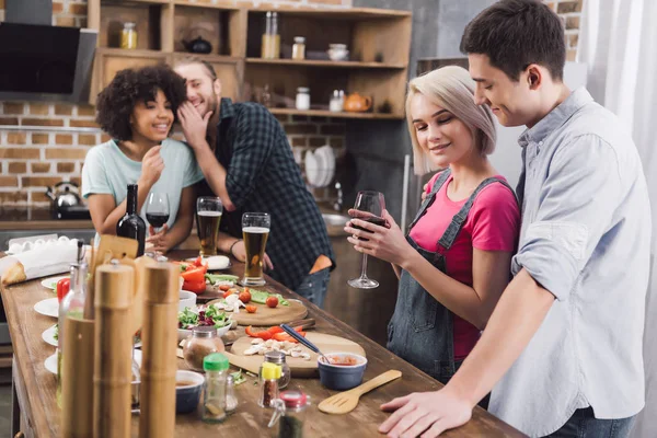 Amis multiethniques commérage sur couple dans la cuisine — Photo de stock