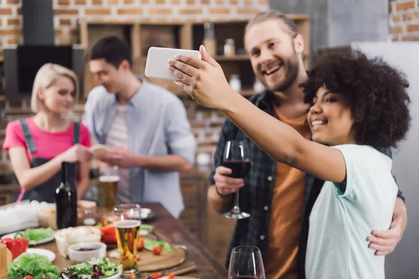 Multiethnic friends taking selfie in kitchen with smartphone — Stock Photo