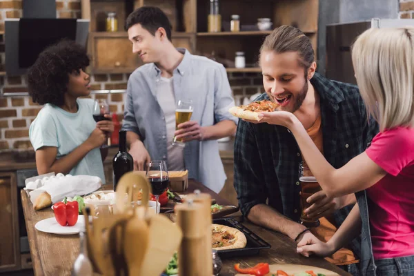 Menina alimentando amigo com pedaço de pizza na cozinha — Fotografia de Stock