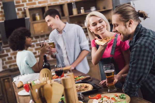 Amigos multiculturais comer pizza caseira e beber álcool em casa — Fotografia de Stock