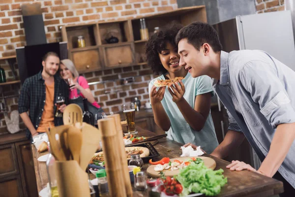 Menina alimentando amigo com pedaço de pizza na cozinha — Fotografia de Stock