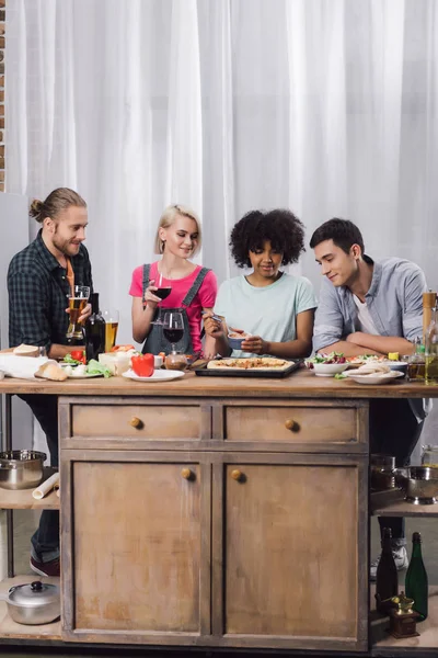 Amigos multiculturais comer pizza caseira e beber álcool em casa — Fotografia de Stock