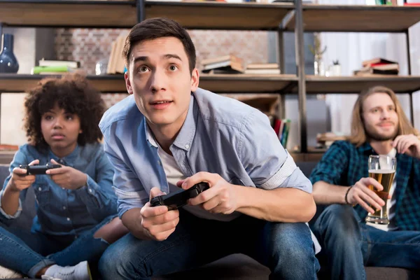 Amigos multiculturales jugando videojuego en el sofá en casa - foto de stock