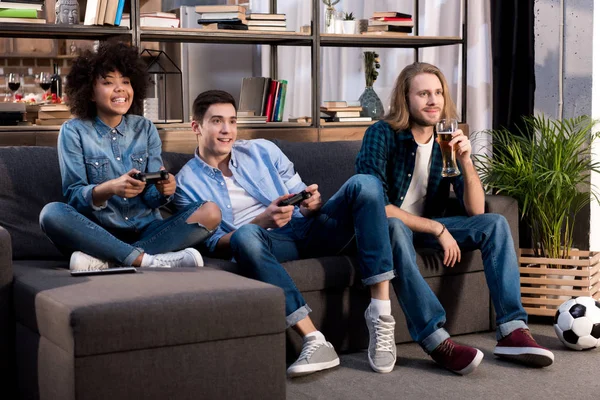 Amici multiculturali che giocano al videogioco sul divano di casa — Foto stock