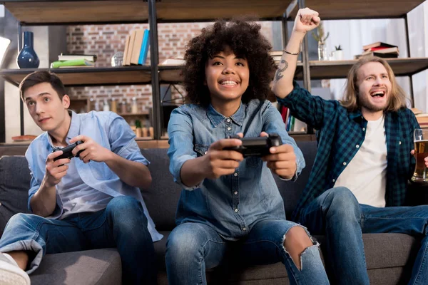 Multicultural friends playing video game on sofa at home — Stock Photo