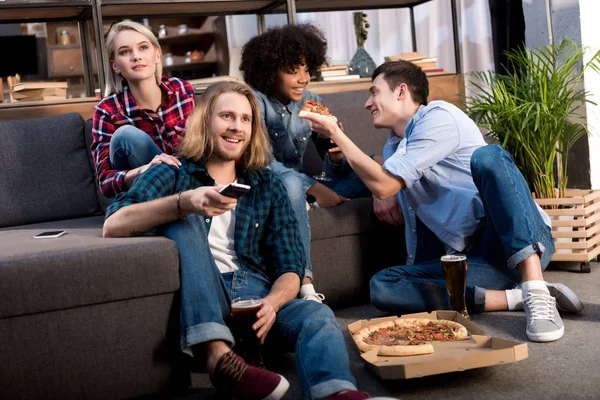 Multicultural friends watching tv and eating pizza at home — Stock Photo