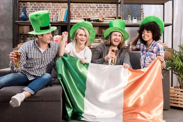 Happy multicultural friends watching tv on saint patrick day with irish flag — Stock Photo