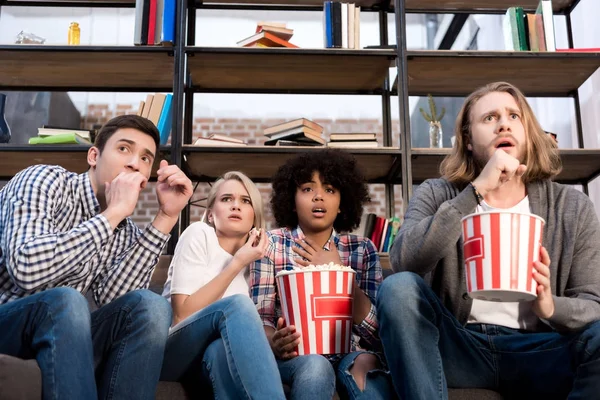 Geschockte multiethnische Freunde sehen Horrorfilm mit Popcorn — Stockfoto