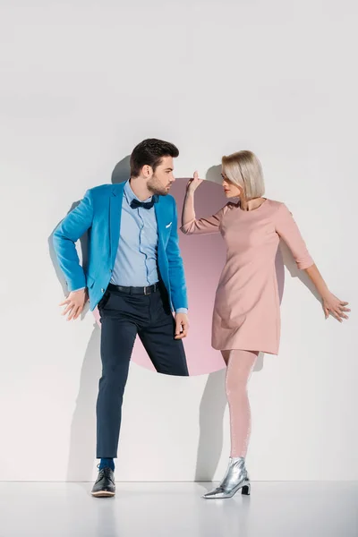 Beautiful fashionable couple in love looking at each other while standing together in aperture on grey — Stock Photo