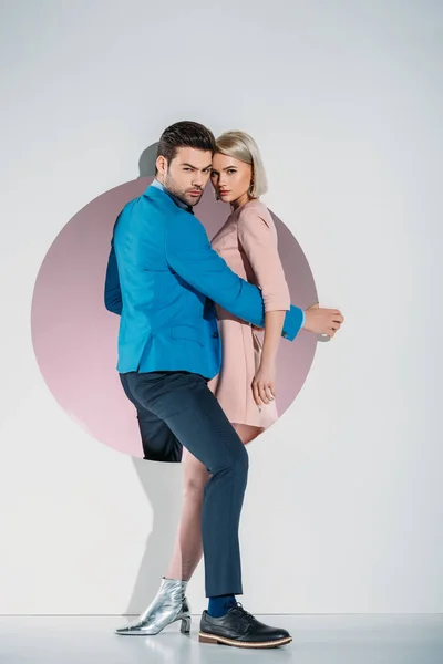 Hermosa pareja joven con estilo en el amor mirando a la cámara, mientras que de pie juntos en el agujero en gris - foto de stock