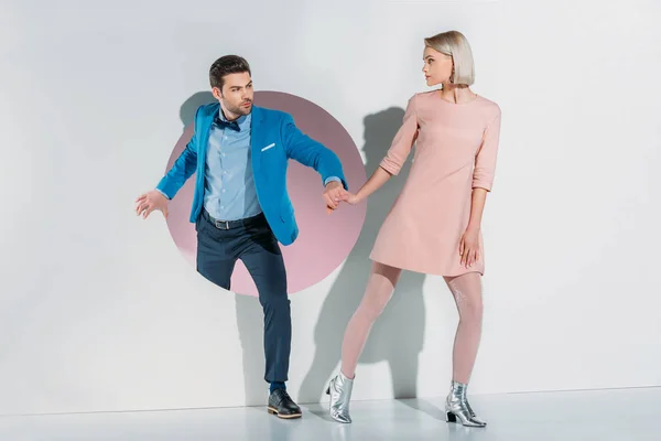 Young couple in suit and dress holding hands and looking at each other on grey — Stock Photo