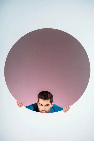 Stylish bearded young man looking at camera through hole on grey — Stock Photo