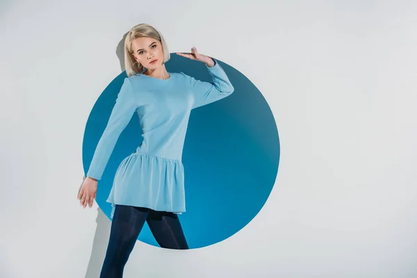 Linda menina loira em vestido azul olhando para a câmera e posando em buraco no cinza — Fotografia de Stock