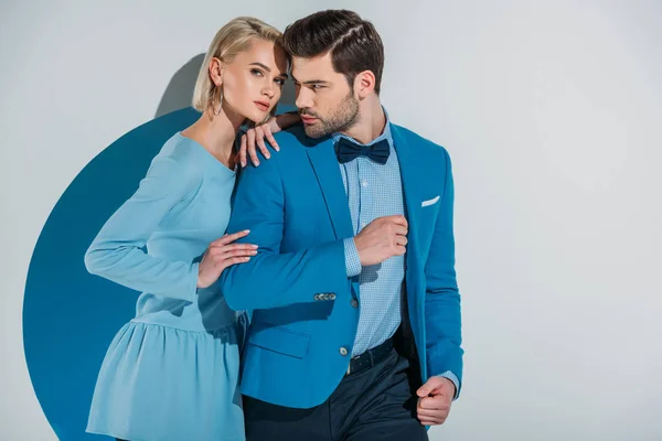 Beautiful couple in stylish blue suit and dress standing together in aperture on grey — Stock Photo