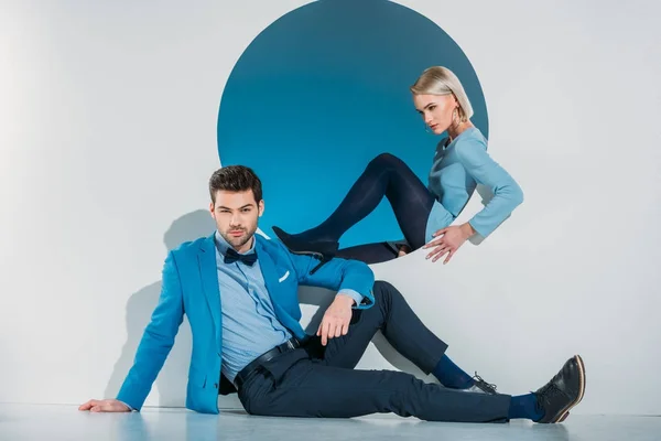 Schönes stylisches junges Paar in blauem Anzug und Kleid sitzt in der Nähe der Öffnung auf grau — Stockfoto