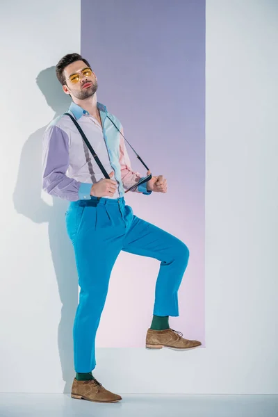 Beau jeune homme élégant dans les bretelles et les lunettes debout dans l'ouverture sur gris — Photo de stock