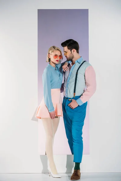 Vue latérale du jeune couple à la mode en lunettes de soleil debout ensemble dans l'ouverture sur le gris — Photo de stock