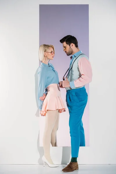 Fashionable young couple in eyeglasses looking at each other while standing in aperture on grey — Stock Photo