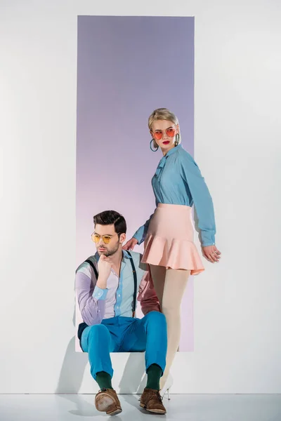 Hermosa pareja joven con estilo en gafas de sol posando juntos en la apertura en gris - foto de stock