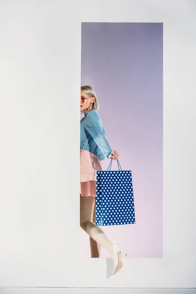 Stylische junge Frau mit Einkaufstasche tritt durch die Blende auf grau — Stockfoto