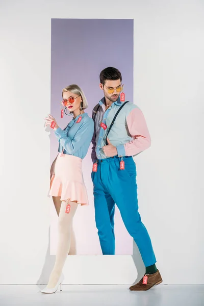 Full length view of stylish young couple with sale tags on clothes standing in opening on grey — Stock Photo