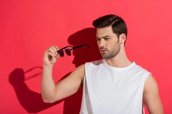 Handsome bearded young man holding sunglasses on pink — Stock Photo