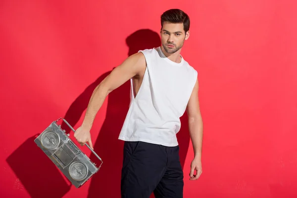 Handsome young man holding tape recorder and looking at camera on pink — Stock Photo