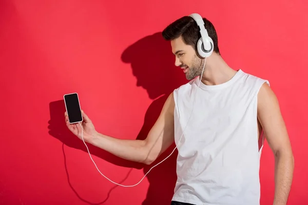 Apuesto joven sonriente en auriculares escuchando música con teléfono inteligente en rosa - foto de stock