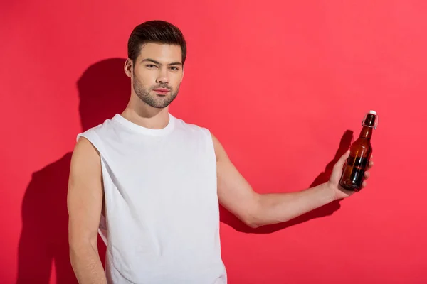 Handsome young man holding beer bottle and looking at camera on pink — Stock Photo