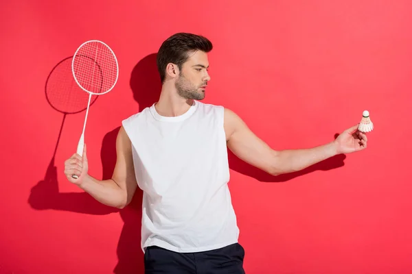 Joven guapo sosteniendo raqueta de bádminton y volante en rosa - foto de stock