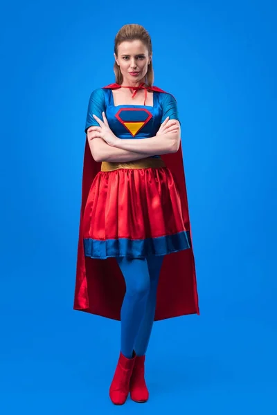 Atractiva mujer en traje de superhéroe con los brazos cruzados aislados en azul - foto de stock