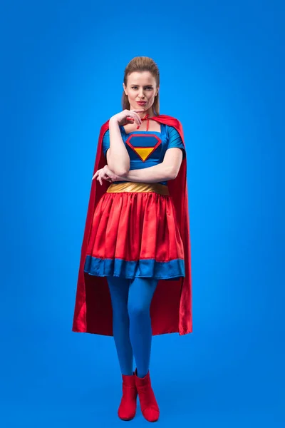 Mujer reflexiva en traje de superhéroe mirando a la cámara aislada en azul - foto de stock