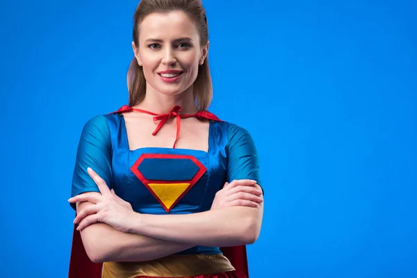 Retrato de mujer sonriente en traje de superhéroe con los brazos cruzados aislados en azul - foto de stock