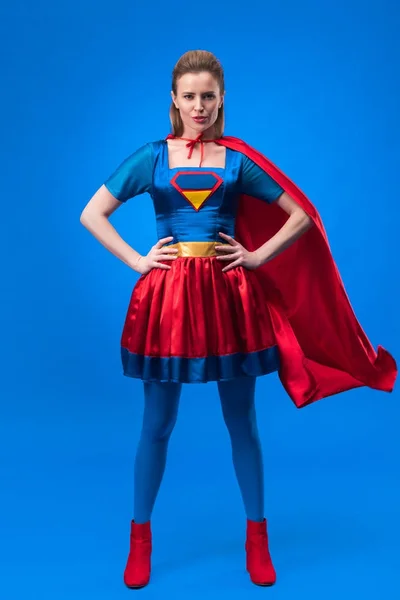 Bela mulher confiante em traje de super-herói de pé akimbo isolado em azul — Fotografia de Stock