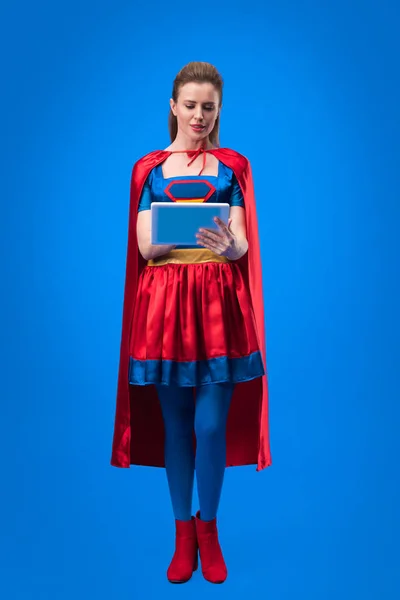 Donna caucasica in costume da supereroe utilizzando tablet isolato su blu — Foto stock