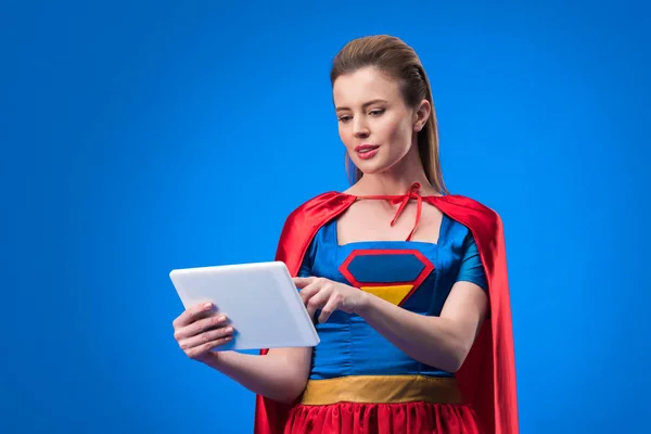 Portrait de femme caucasienne en costume de super-héros en utilisant une tablette isolée sur bleu — Photo de stock