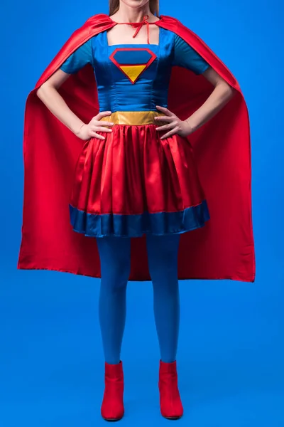 Vista parcial de la mujer en traje de superhéroe de pie akimbo aislado en azul - foto de stock