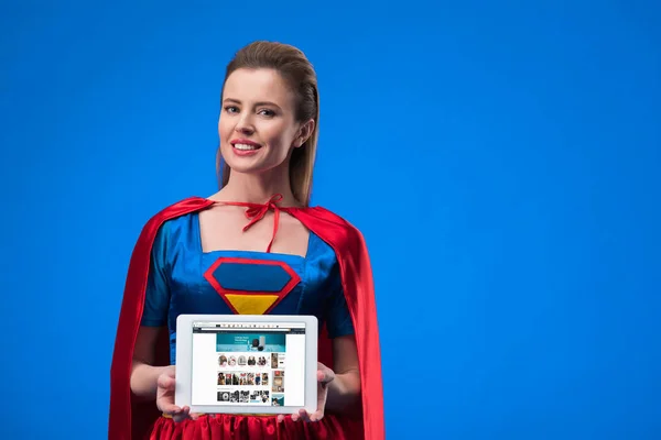 Portrait of cheerful woman in superhero costume showing tablet isolated on blue — Stock Photo