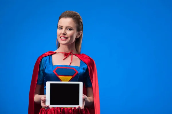 Portrait de femme souriante en costume de super-héros montrant tablette avec écran blanc isolé sur bleu — Photo de stock