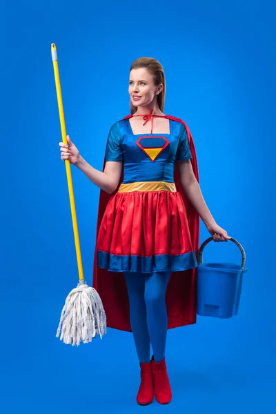 Mulher atraente em traje de super-herói com esfregona e balde para limpeza isolada em azul — Fotografia de Stock