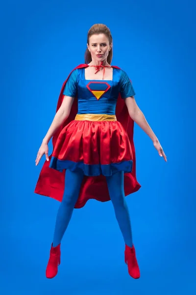 Красива супер жінка в костюмі стрибає ізольовано на синьому — стокове фото
